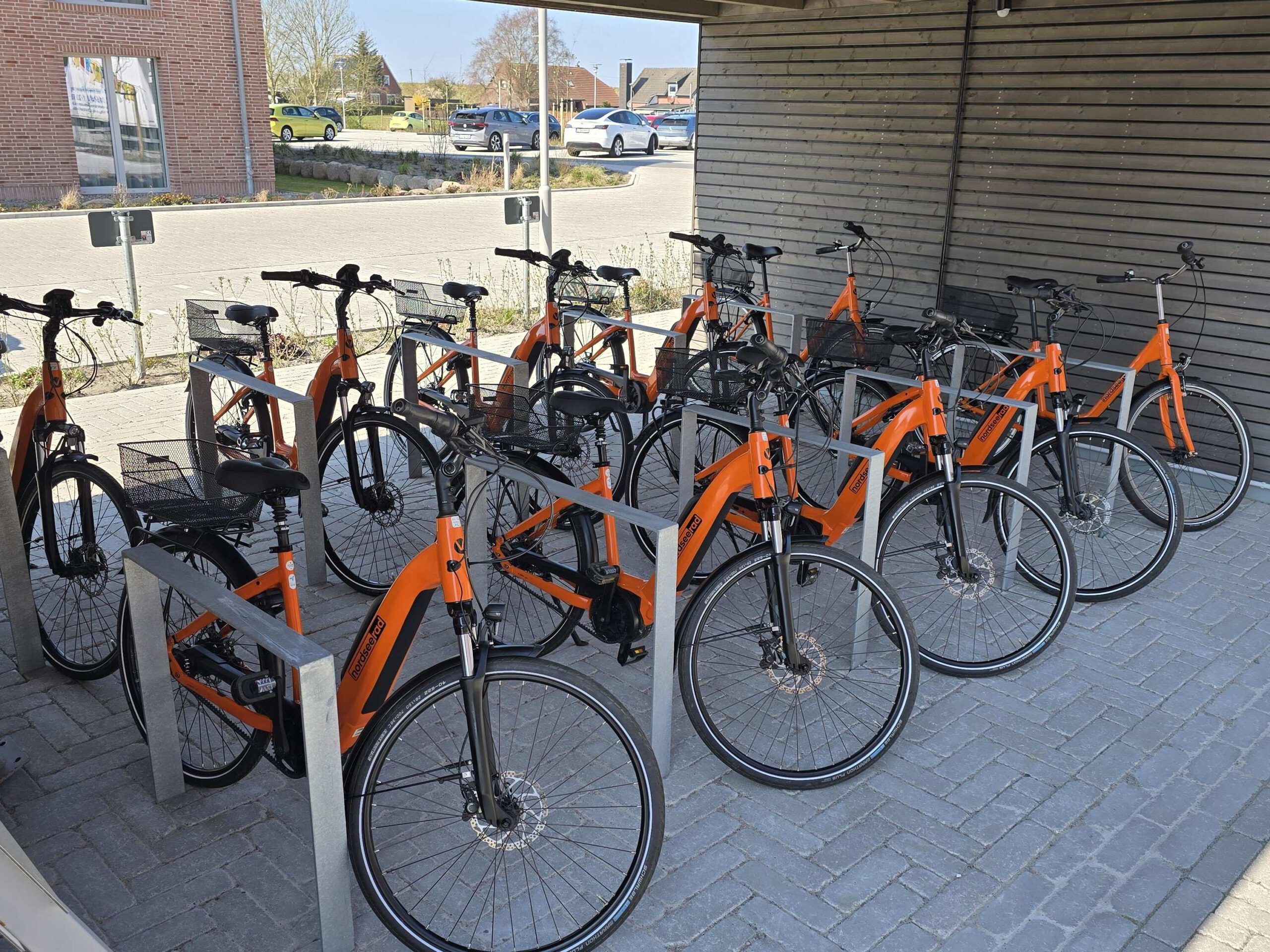 Fahrradverleih: NordseeRad Partnerstation Carolinensiel.  E-Bikes und NordseeRäder. Fahrräder stehen geordnet an Fahrradständern.