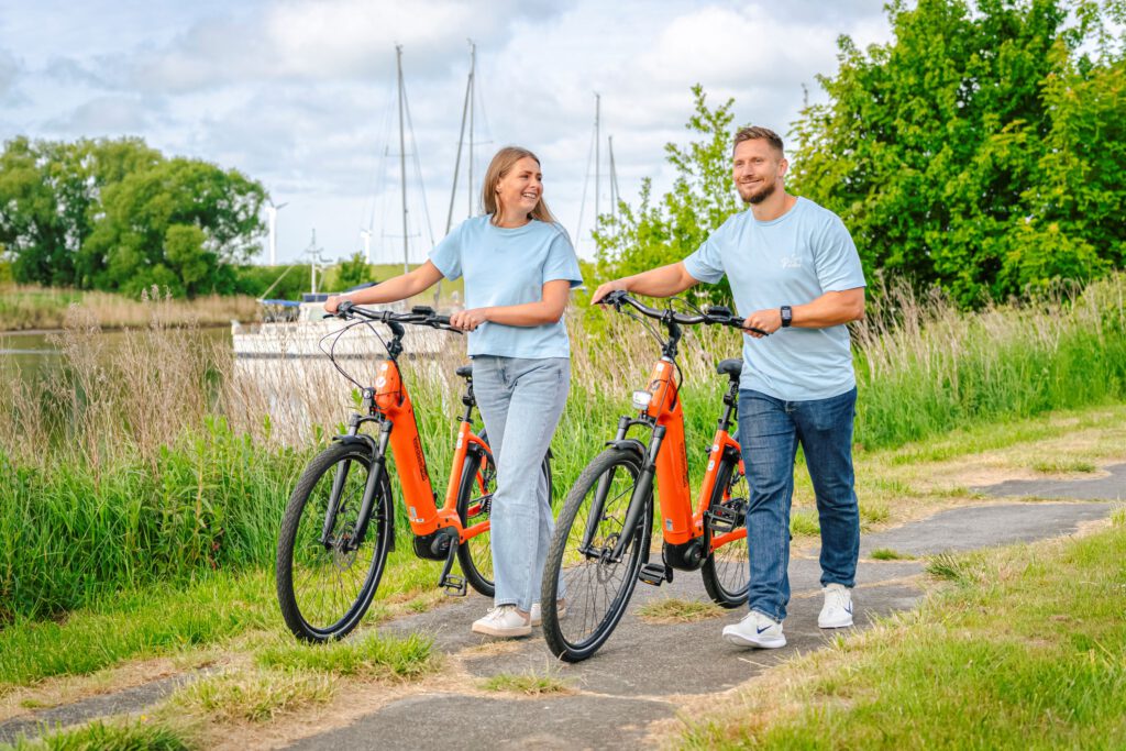 Paar schiebt Nordseeräder vor Bootkulisse